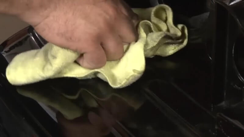 A mechanic wiping away dust and debris from the empty headlight socket with a microfiber cloth
