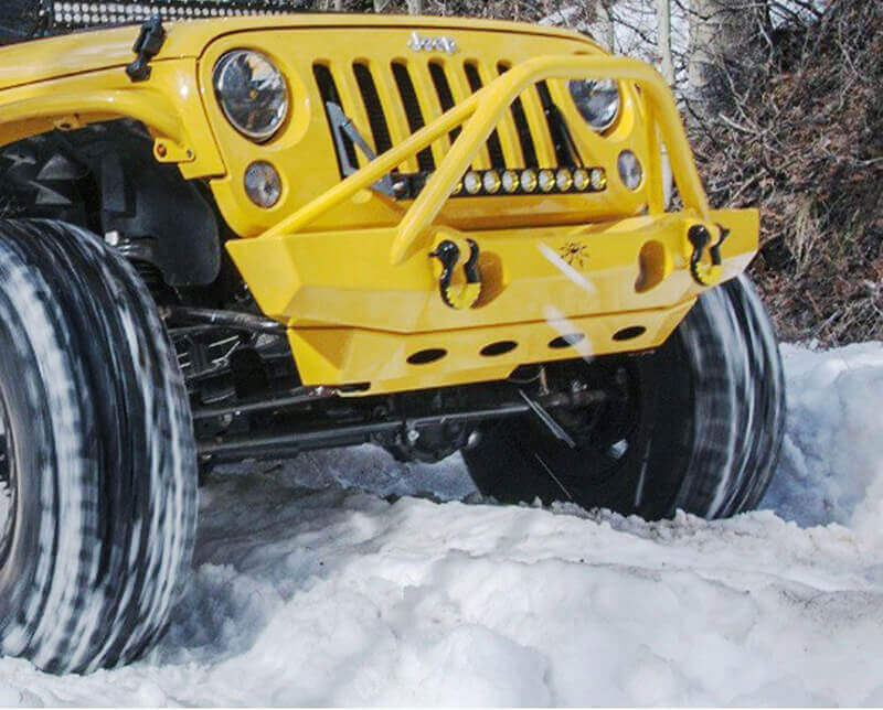 A yellow Jeep with a bumper mounted light bar in the snow