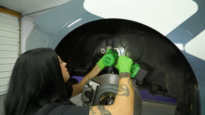 A mechanic unscrewing the upper and lower rear shock mount bolts with a drill