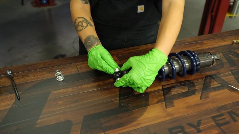 A mechanic pushing round metal spacers into place at the top of the coilover