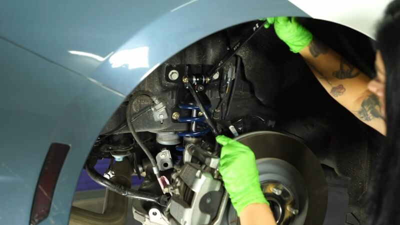A mechanic tightening down a coilover mounting bolt with two wrenches