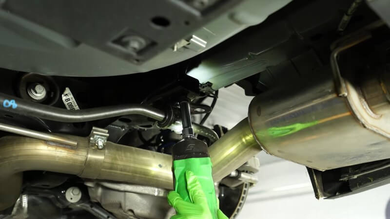 A mechanic unbolting the factory sway bar mounting bracket with an impact wrench