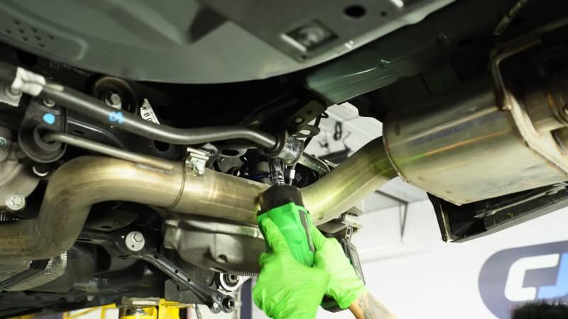 A mechanic bolting the new sway bar mounting plate to the chassis with an impact wrench