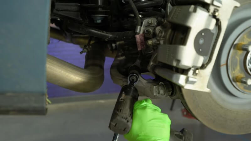 A mechanic using a drill to loosen and disconnect the rear sway bar end link
