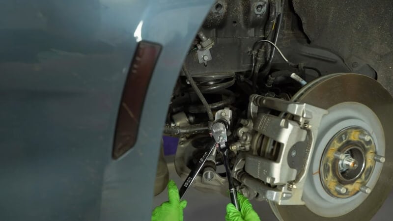 A mechanic using two wrenches to loosen the top sway bar end link bolt