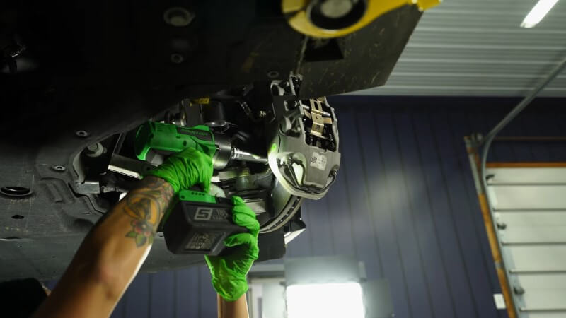 A mechanic using an impact wrench to remove the bolts holding the brake caliper in place