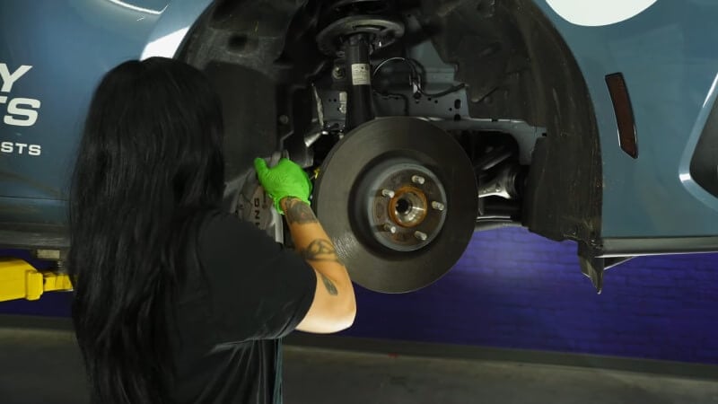 A mechanic tucking the brake caliper out of the way to access the brake rotor