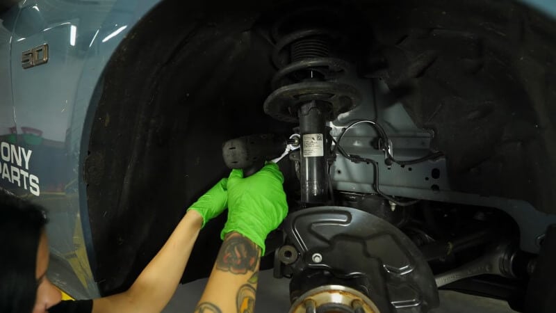 A mechanic using an impact and socket wrench removing the front sway bar link