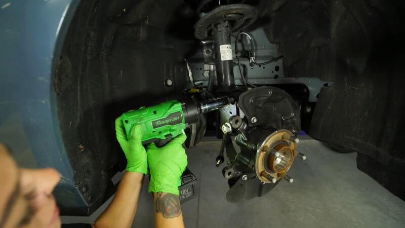 A mechanic using an impact wrench to remove the bolts holding the strut to the wheel hub assembly