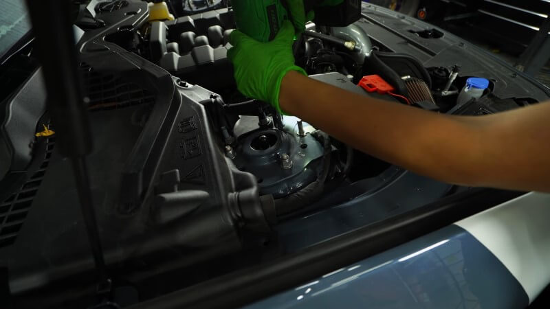 A mechanic using an impact wrench to remove the strut nuts on the top of the strut tower