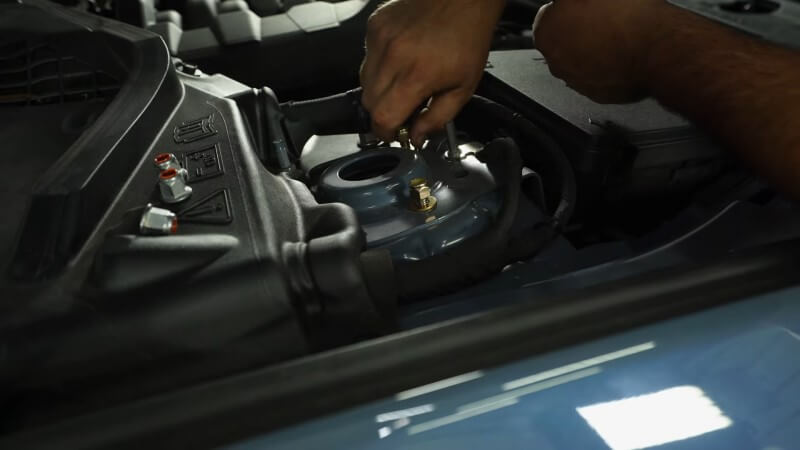 A mechanic hand tightening strut nuts onto the exposed studs poking out of the strut tower