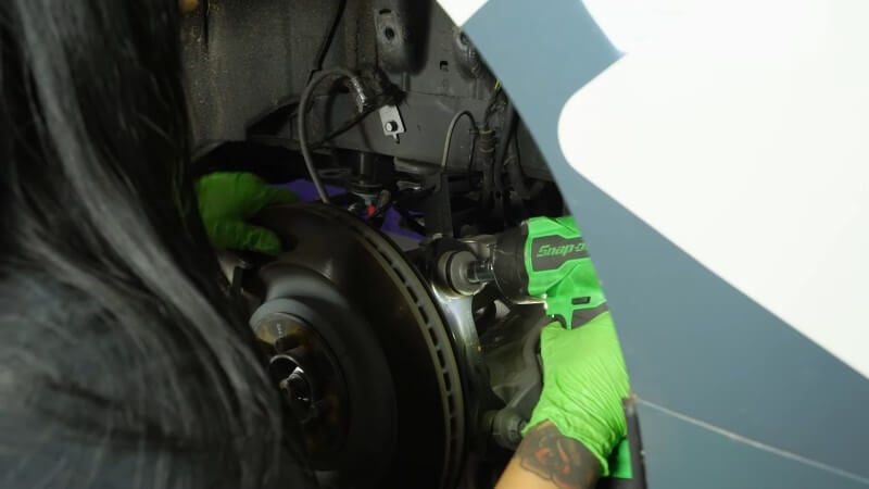 A mechanic using a drill to remove spring mounting bolts