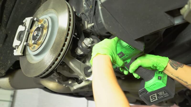 A mechanic using a drill to remove spring mounting bolts