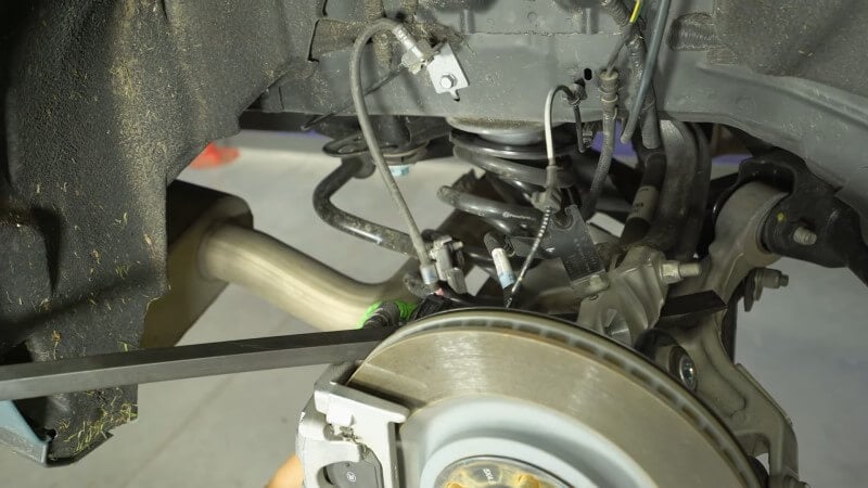 A mechanic removing the rear coil spring in a 2024 Mustang GT