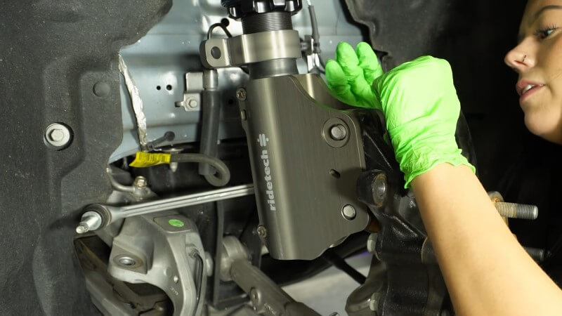 A mechanic pushing the factory strut mounting bolts into place on the bottom of the new coilover