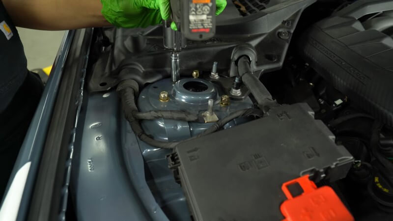 A mechanic using an impact wrench to tighten down the strut tower nuts
