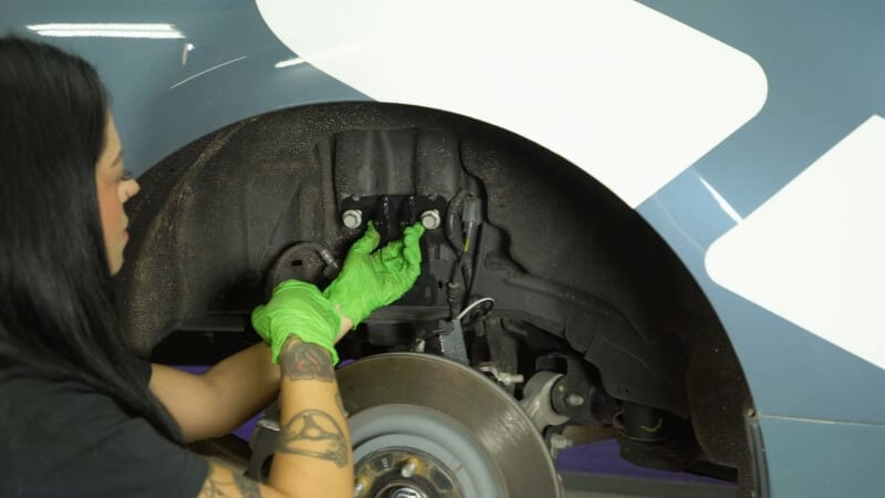 A mechanic hand tightening bolts to hold the upper shock mount in place