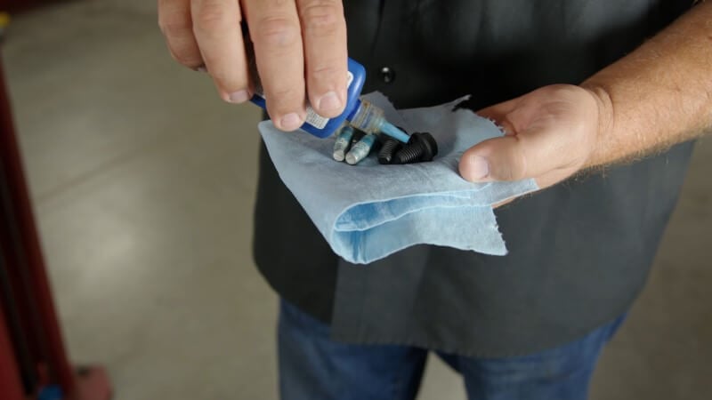Mechanic holding bolts and applying Loctite to them