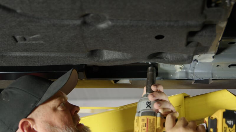 Mechanic bolting the jacking rail into place onto an S650 Mustang
