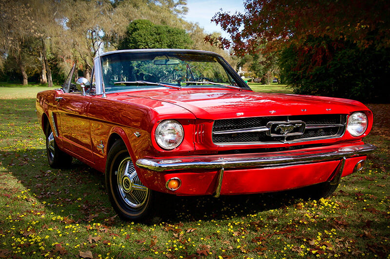 A red classic Mustang convertible parked in a field during fall