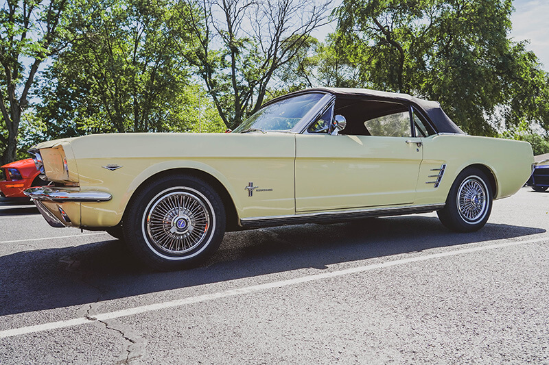 A pale yellow classic Mustang convertible parked in a parking lot at a car show