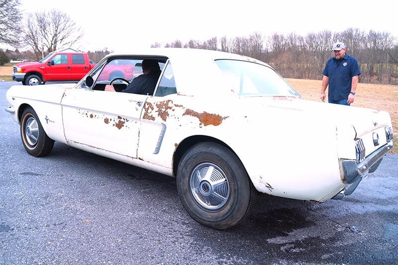 A rusty classic Mustang in a parking lot, ready to go for a drive