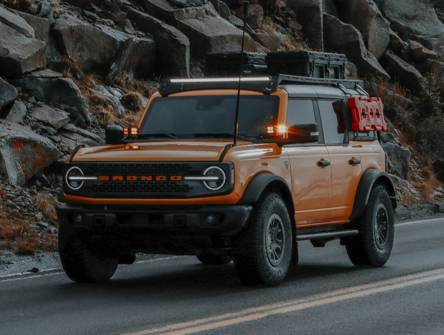 An orange Ford Bronco driving down a two-lane road