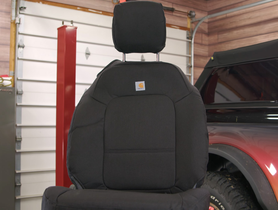 A modern Ford Bronco seat on a table with an aftermarket seat cover equipped
