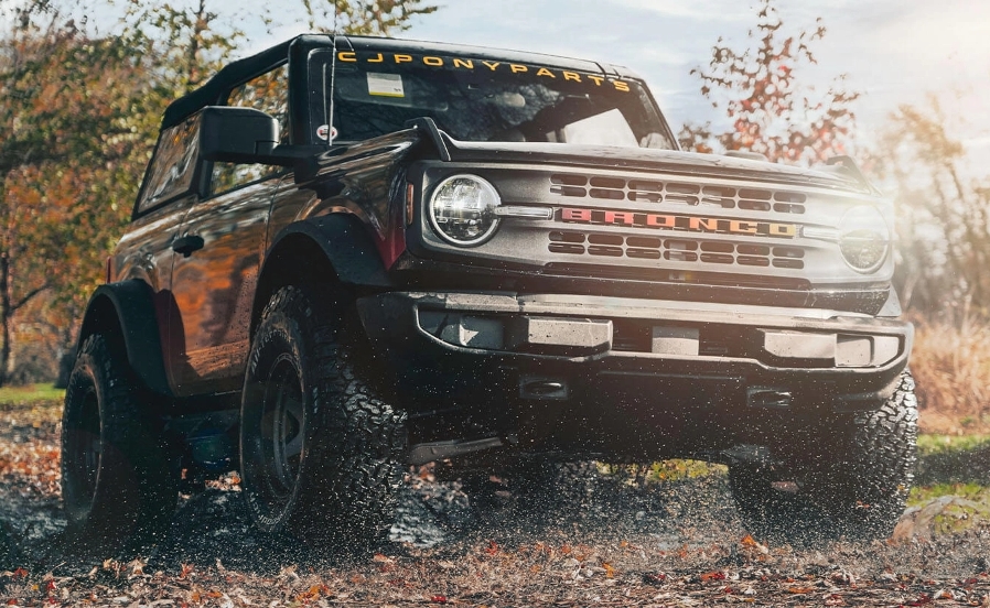 An orange and black Ford Bronco driving through a field in the fall